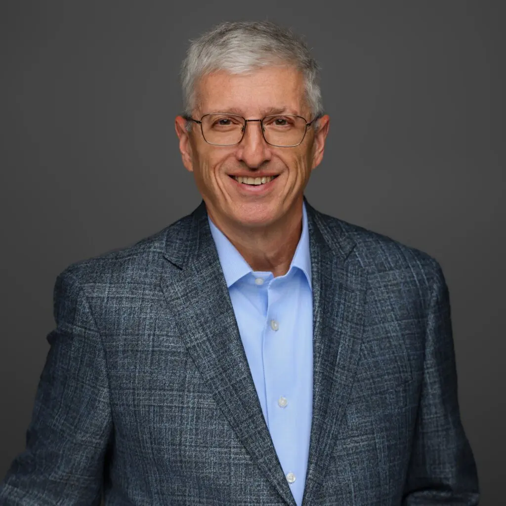 Smiling elderly man with gray hair in a checkered blazer and blue shirt.