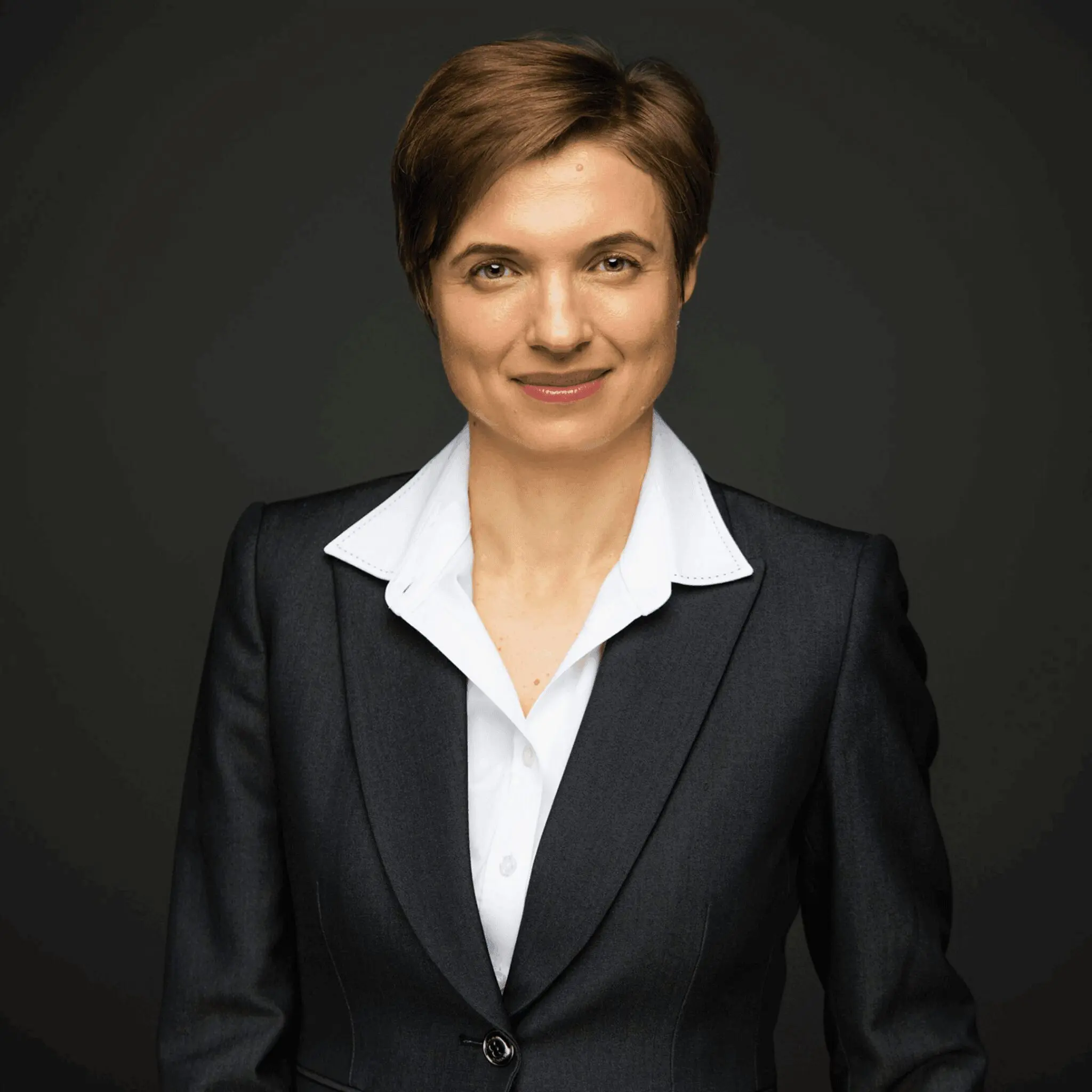 Professional woman in a black blazer against a dark background.