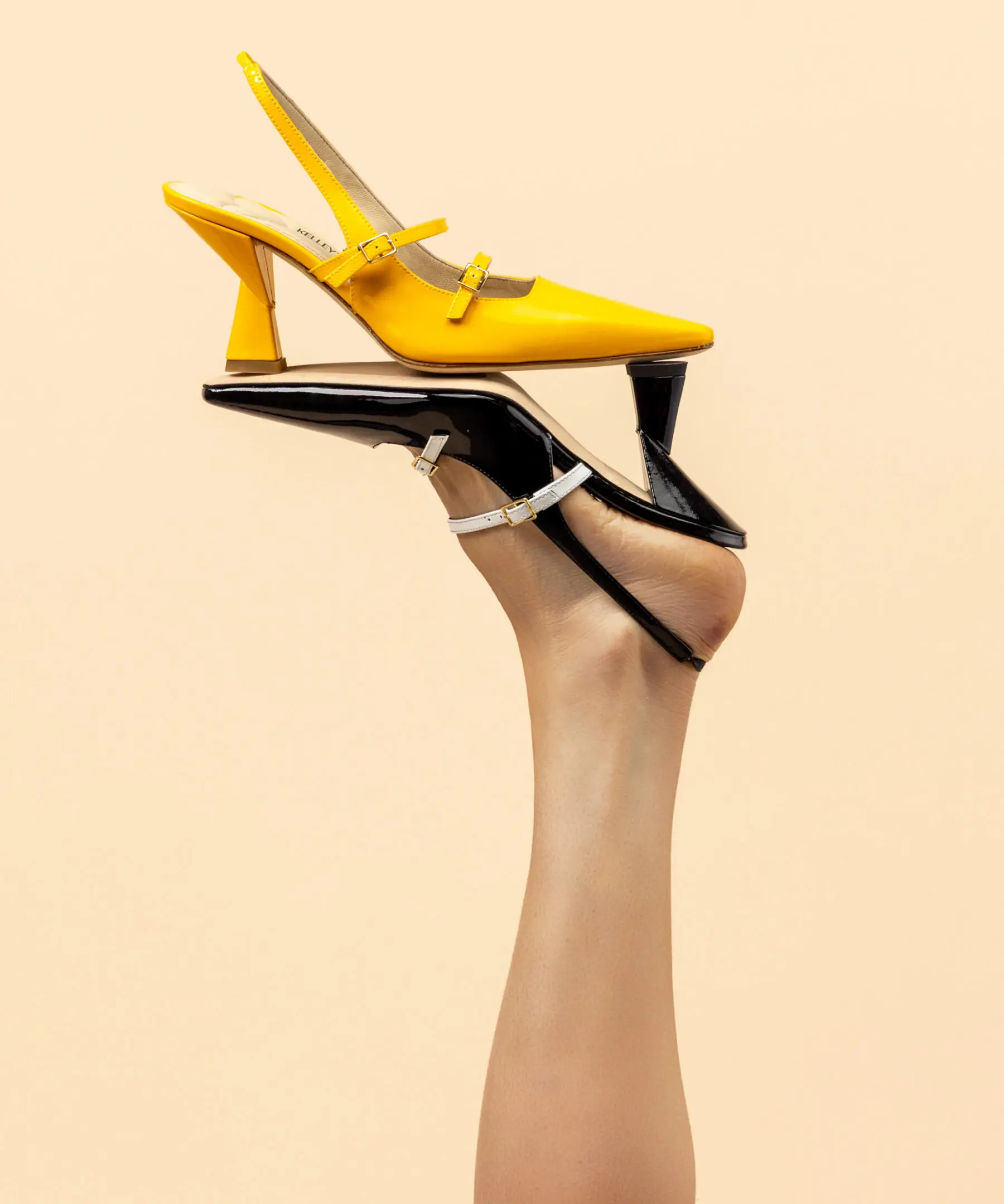 Hands holding a yellow high heel shoe against a beige background.