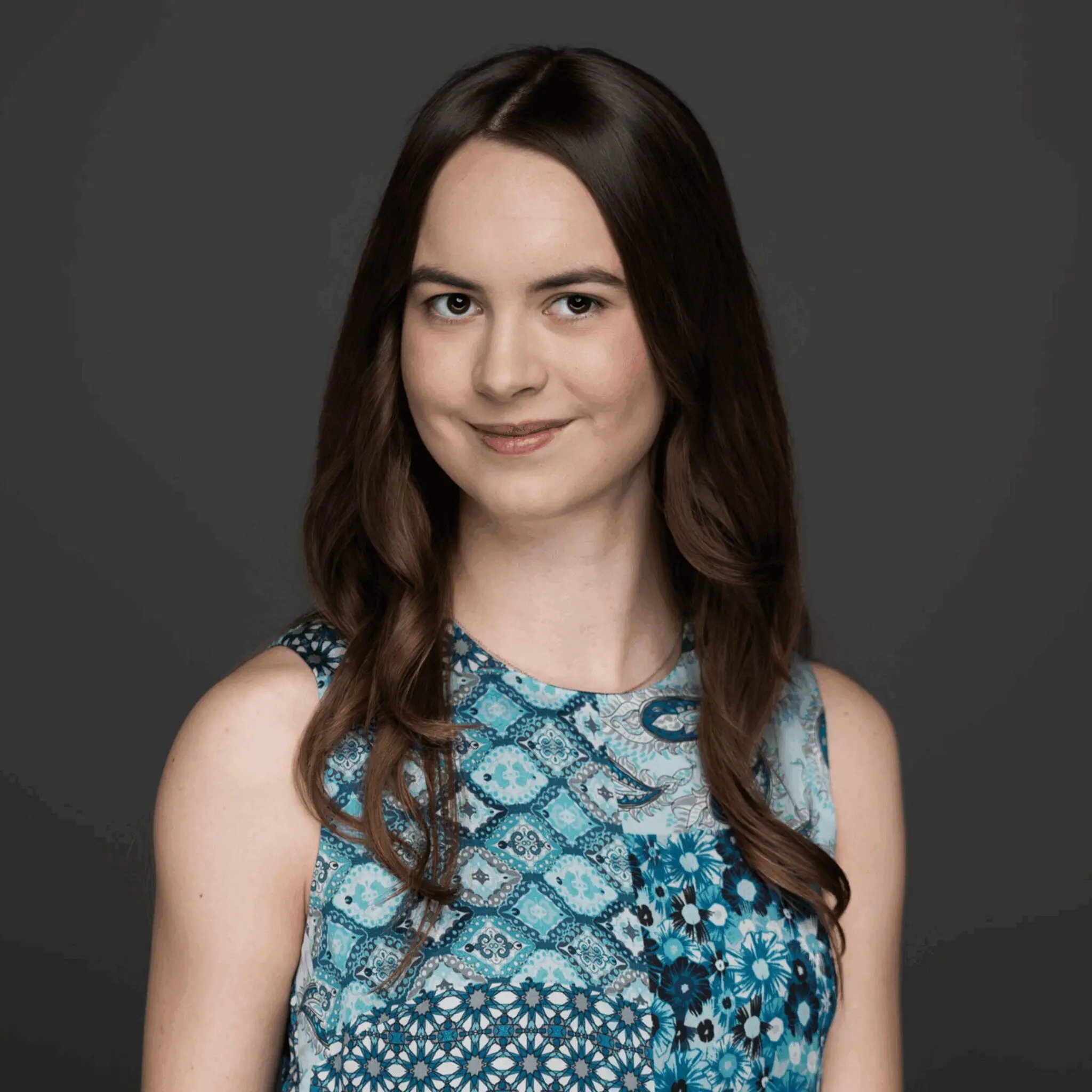 Young woman with long brown hair wearing a blue patterned sleeveless top.