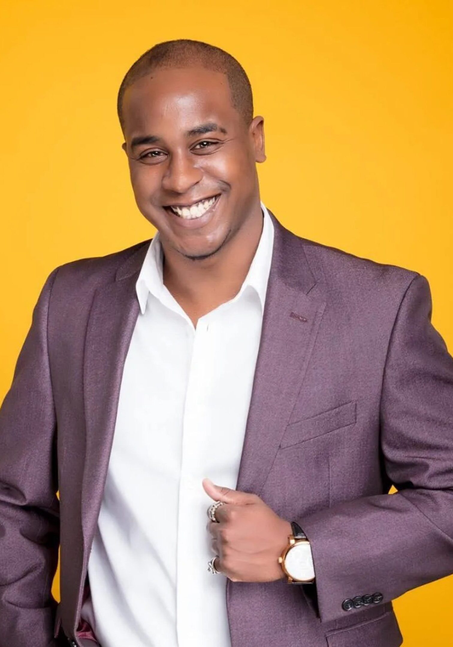 Smiling man in a purple blazer against a yellow background.