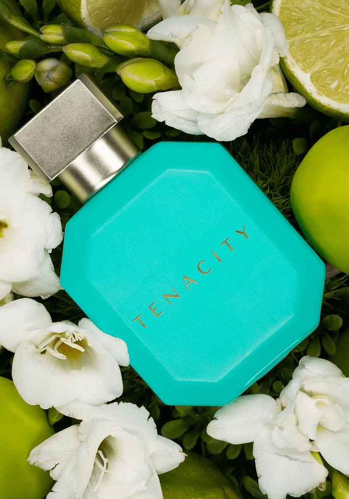 Perfume bottle surrounded by flowers and fruits.